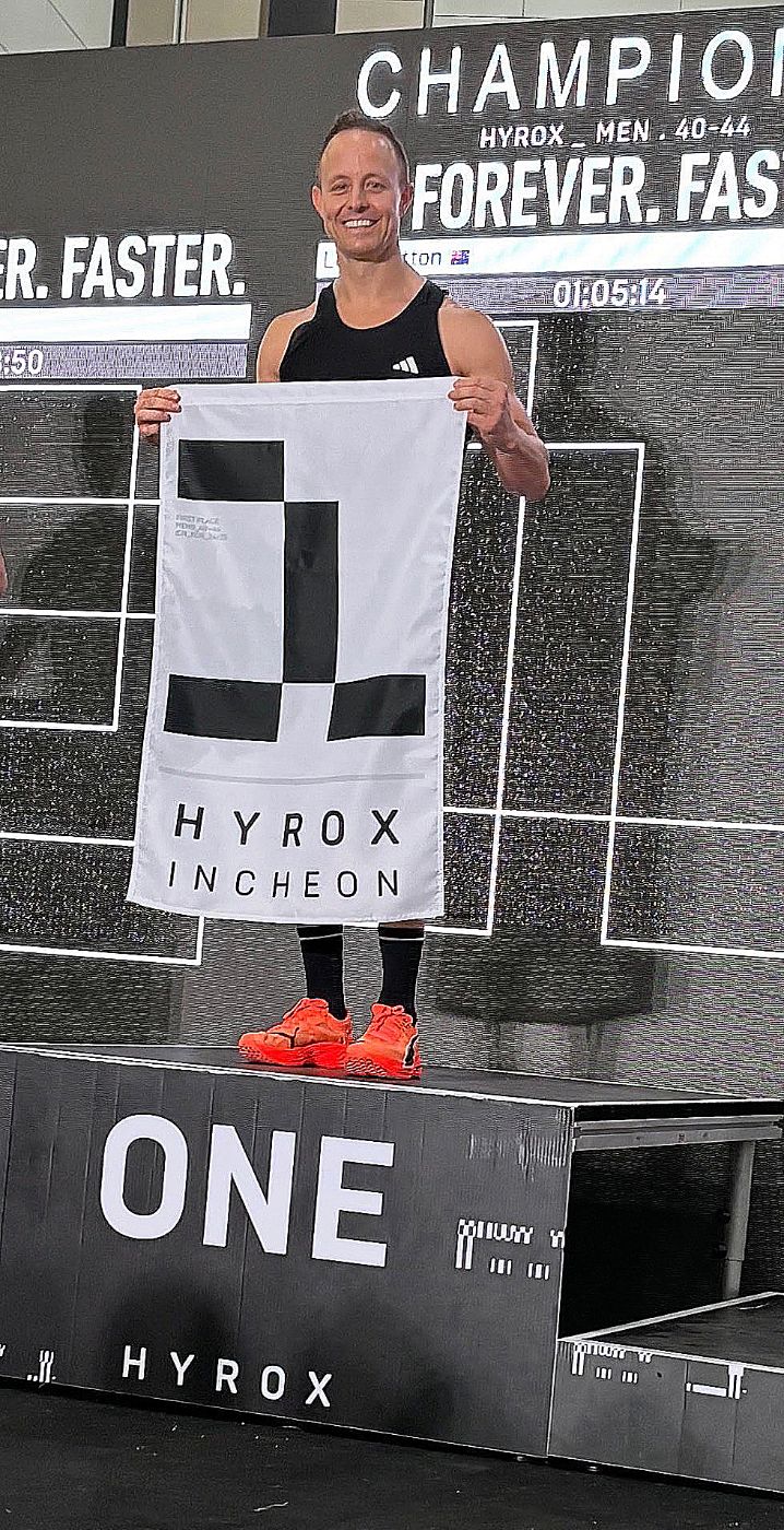 Luke Britton on the podium holding the HYROX Incheon #1 flag