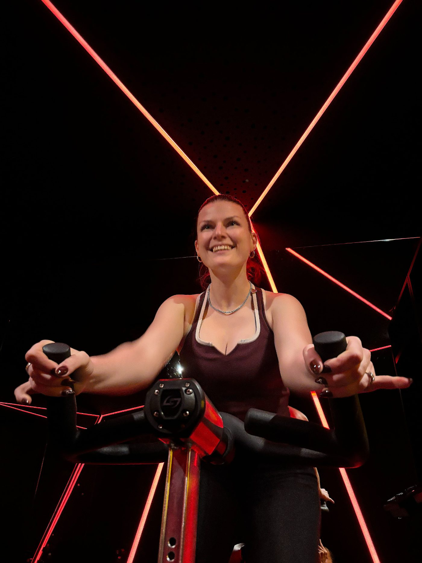 Coach Sophie smiling on a Stages bike under red neon in the Soultrain Ride Room, Woolloomooloo